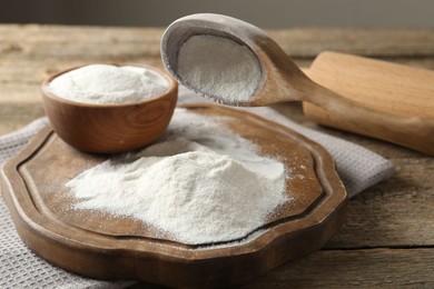 Photo of Wheat flour, spoon and rolling pin on wooden table, closeup