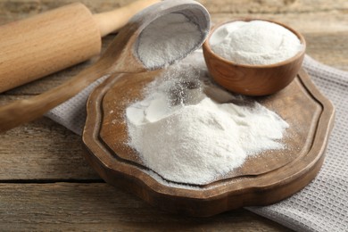 Photo of Wheat flour, spoon and rolling pin on wooden table, closeup