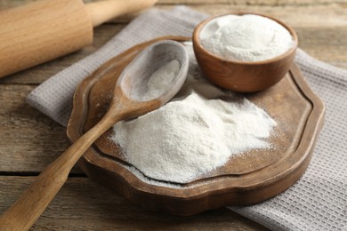 Photo of Wheat flour, spoon and rolling pin on wooden table, closeup