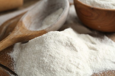 Photo of Wheat flour and spoon on wooden board, closeup