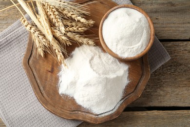 Photo of Wheat flour and spikelets on wooden table, top view
