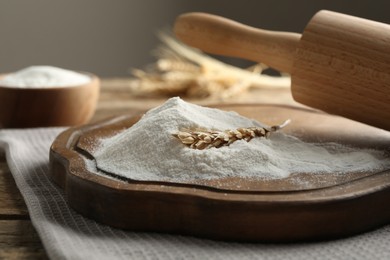 Photo of Wheat flour, spikelet and rolling pin on wooden table, closeup