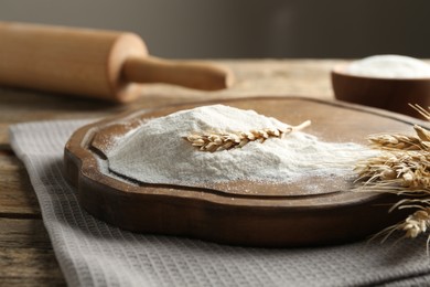 Photo of Wheat flour, spikelets and rolling pin on wooden table, closeup