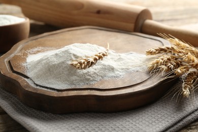 Photo of Wheat flour, spikelets and rolling pin on wooden table, closeup