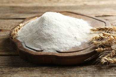Photo of Wheat flour and spikelets on wooden table, closeup