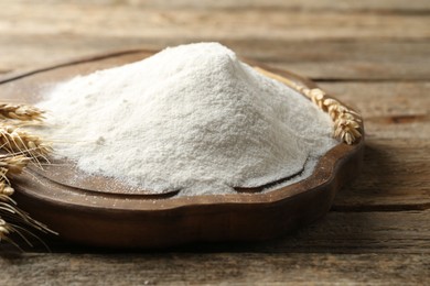 Photo of Wheat flour and spikelets on wooden table, closeup