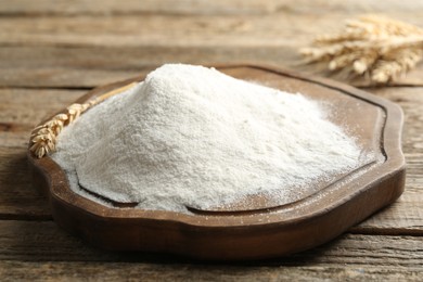 Photo of Wheat flour and spikelets on wooden table, closeup