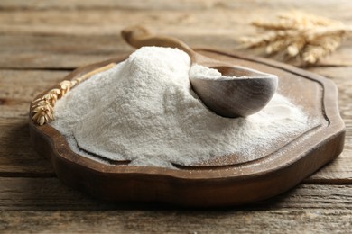 Photo of Wheat flour, spikelets and spoon on wooden table, closeup
