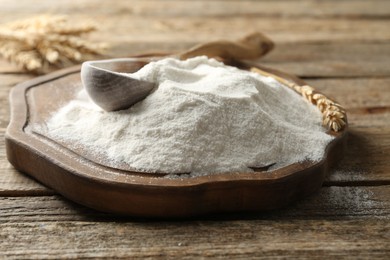 Photo of Wheat flour, spikelets and spoon on wooden table, closeup