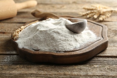 Photo of Wheat flour, spikelets and spoon on wooden table, closeup