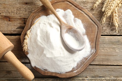 Photo of Wheat flour, spikelets, spoon and rolling pin on wooden table, top view