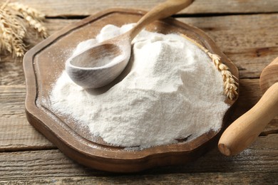 Photo of Wheat flour, spikelets and spoon on wooden table, closeup