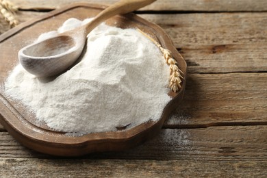 Photo of Wheat flour, spikelet and spoon on wooden table, closeup