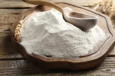 Photo of Wheat flour, spikelet and spoon on wooden table, closeup