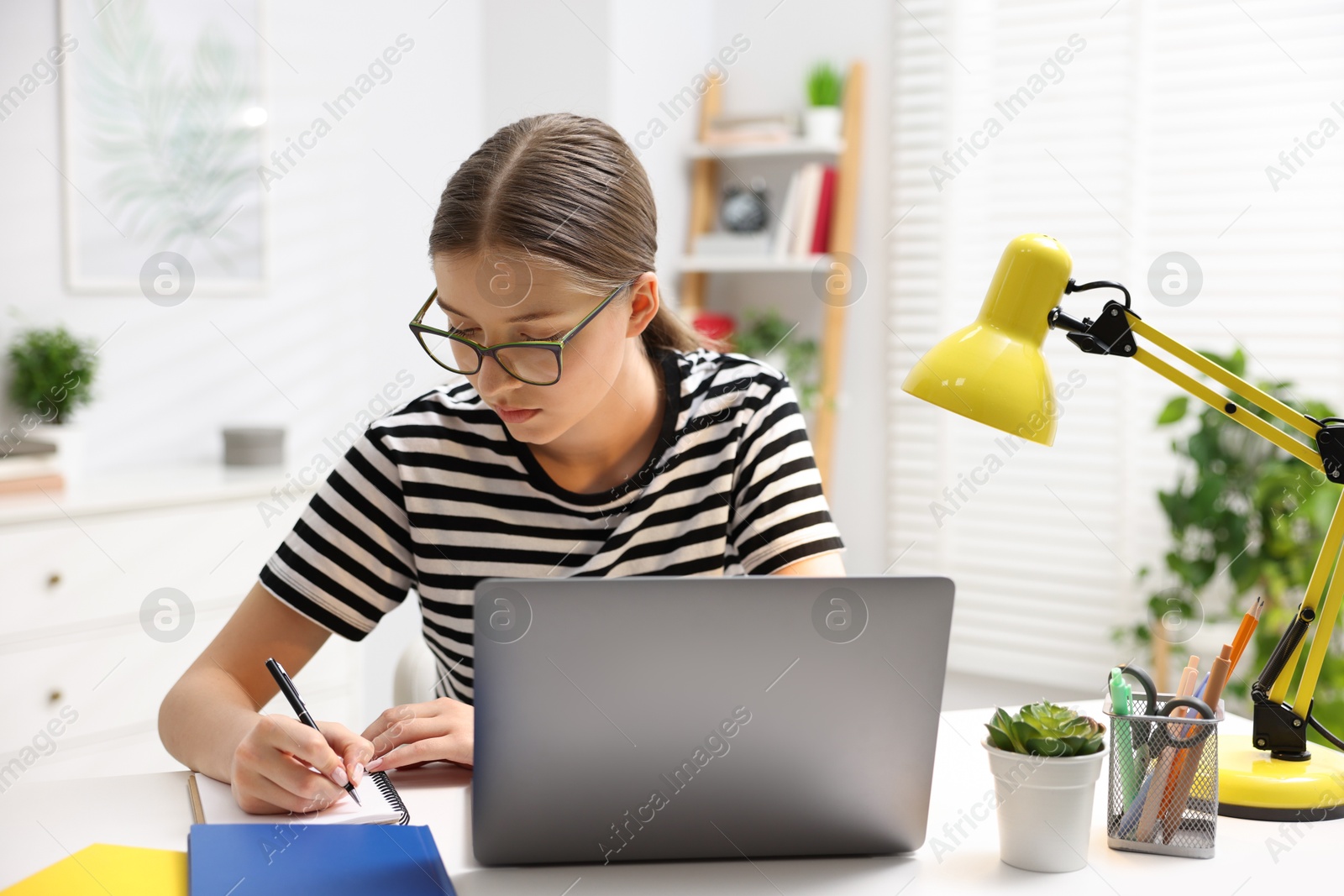 Photo of Teenage girl doing homework with laptop at white desk indoors