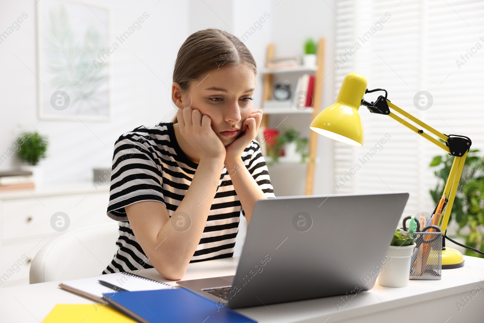 Frustrated teenage girl doing homework with laptop at white desk indoors Photo of Frustrated teenage girl doing homework with laptop at white desk indoors
