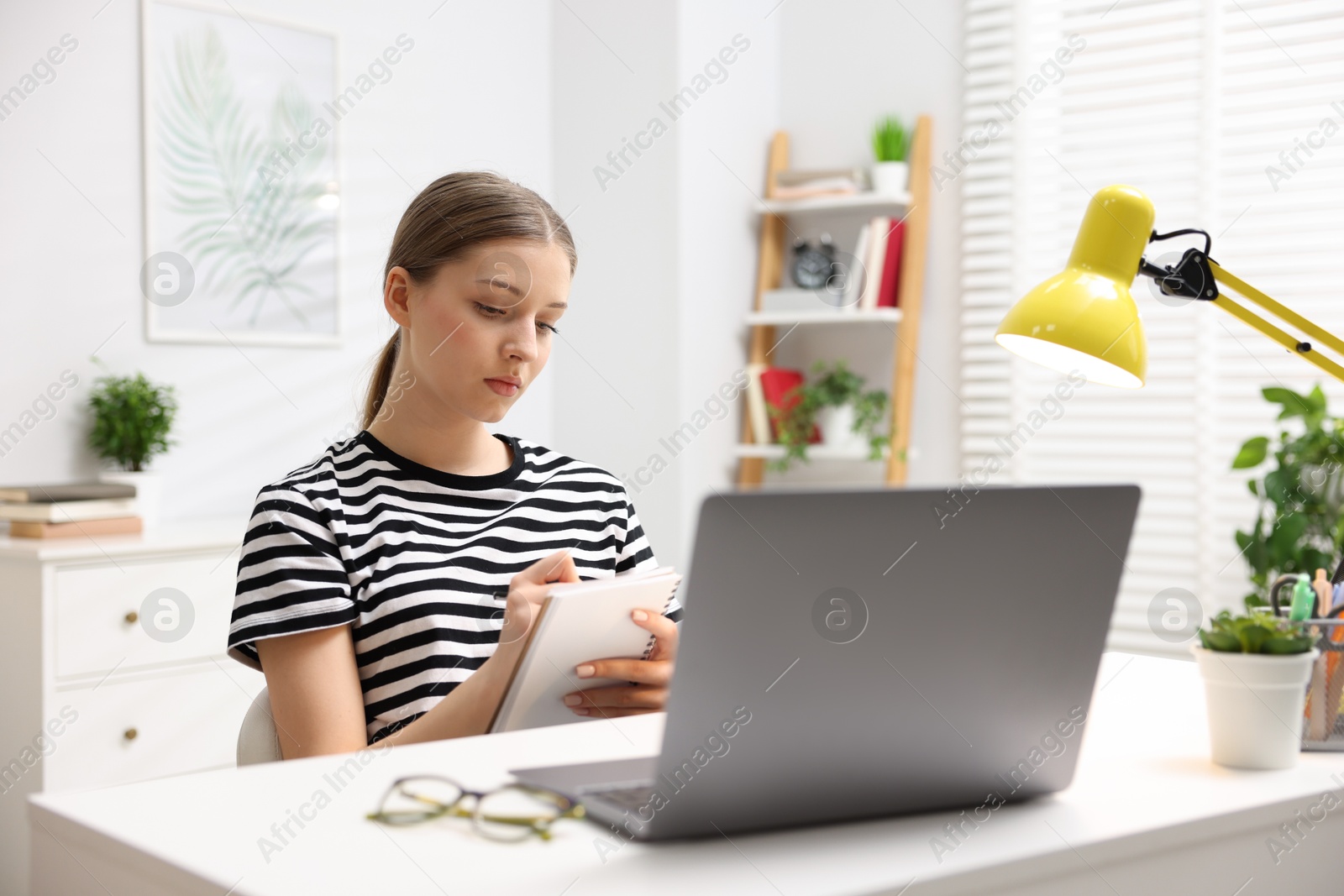 Photo of Teenage girl doing homework with laptop at white desk indoors