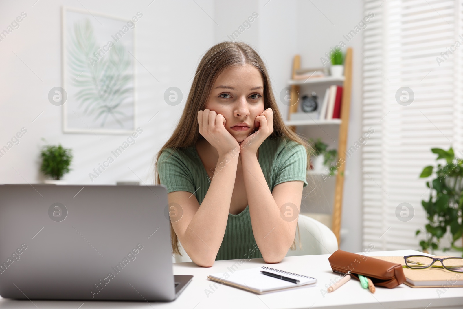 Frustrated teenage girl doing homework with laptop at white desk indoors Photo of Frustrated teenage girl doing homework with laptop at white desk indoors