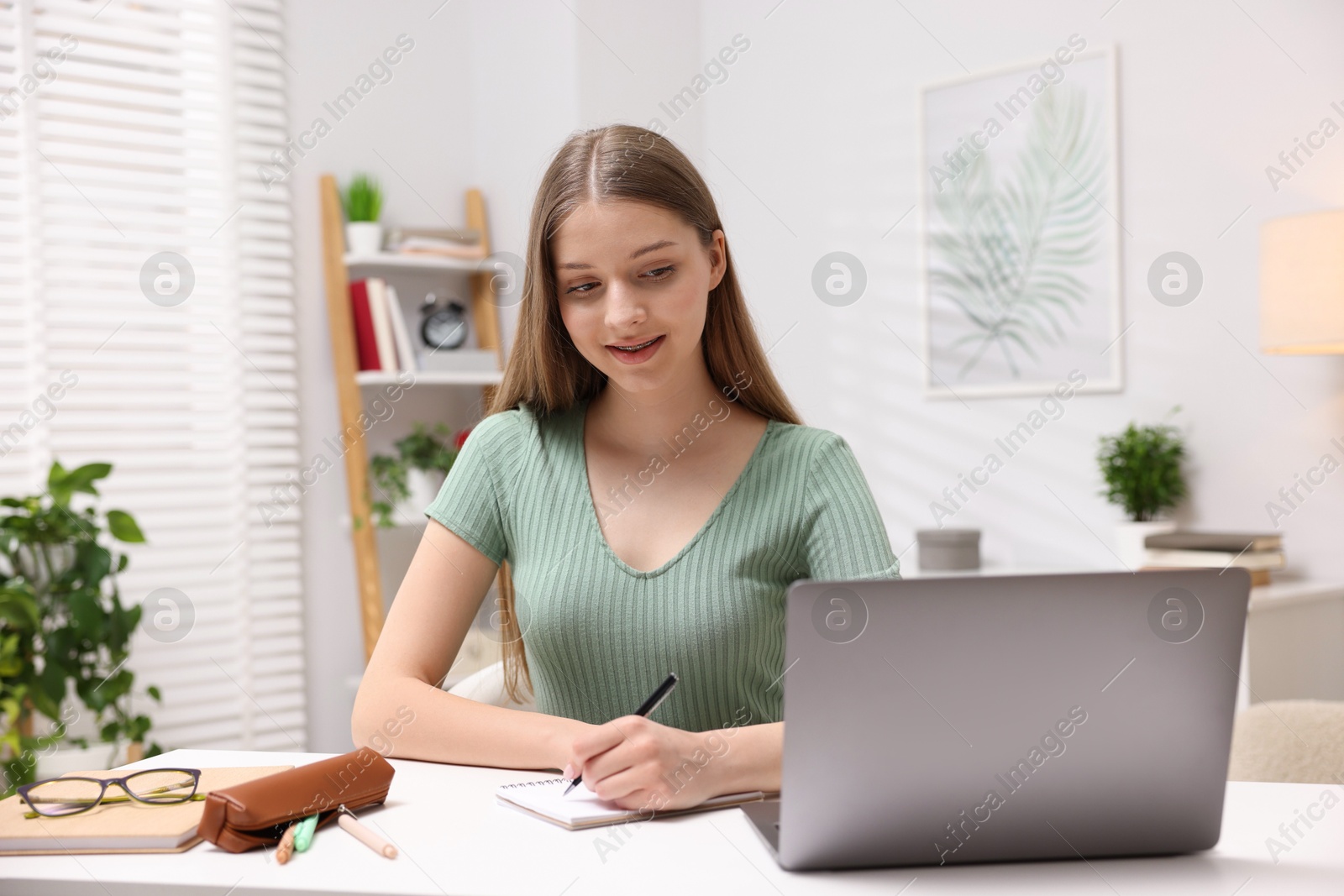 Teenage girl doing homework with laptop at white desk indoors Photo of Teenage girl doing homework with laptop at white desk indoors