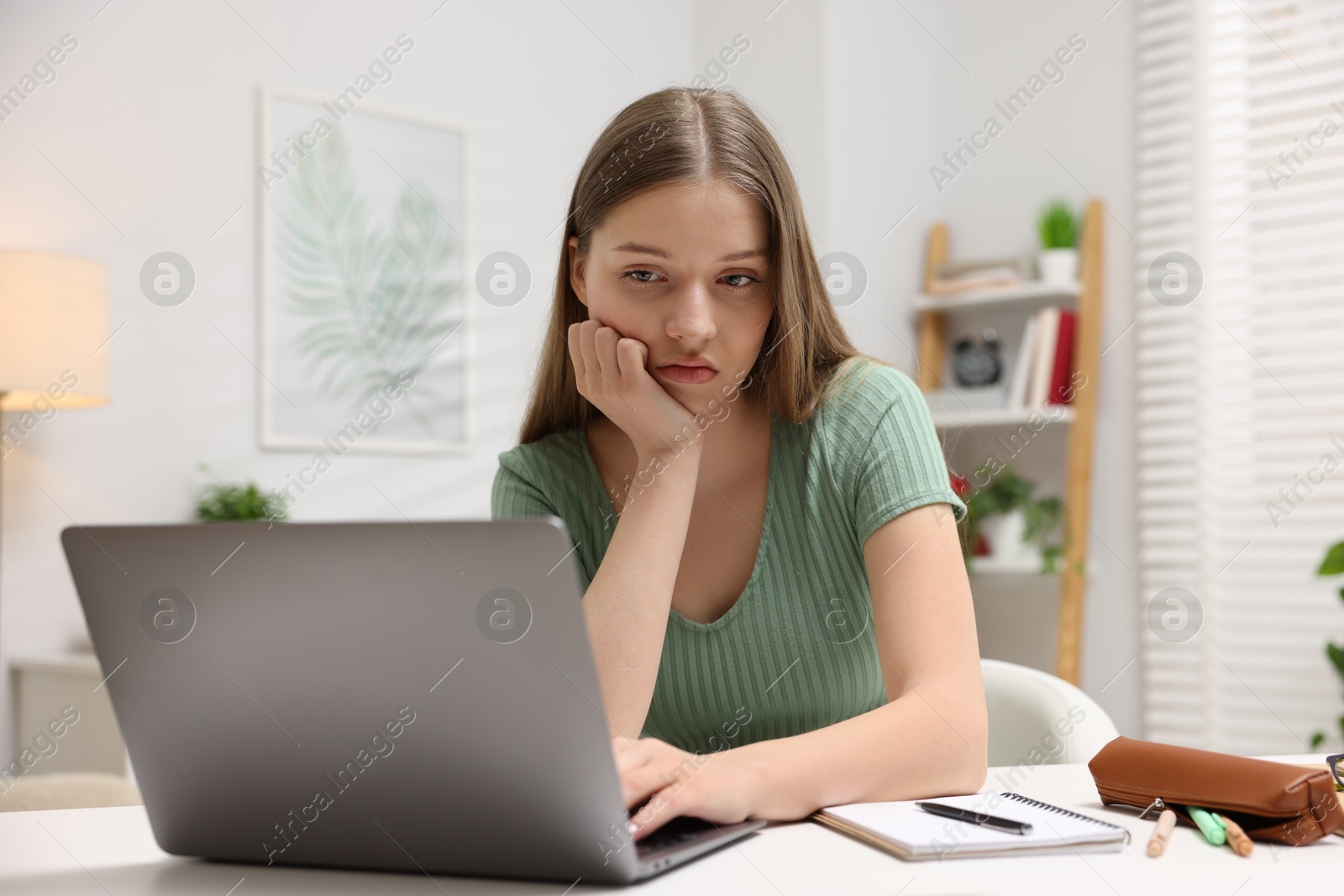 Frustrated teenage girl doing homework with laptop at white desk indoors Photo of Frustrated teenage girl doing homework with laptop at white desk indoors