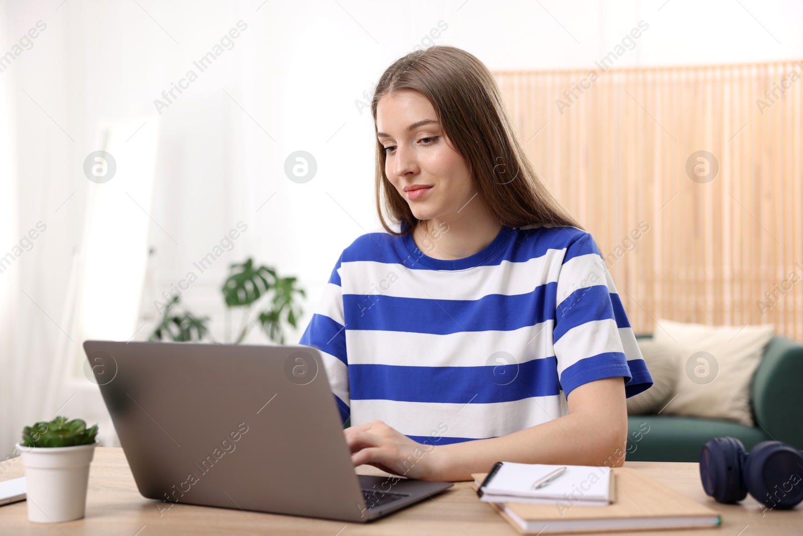 Teenage girl doing homework with laptop at wooden desk indoors Photo of Teenage girl doing homework with laptop at wooden desk indoors