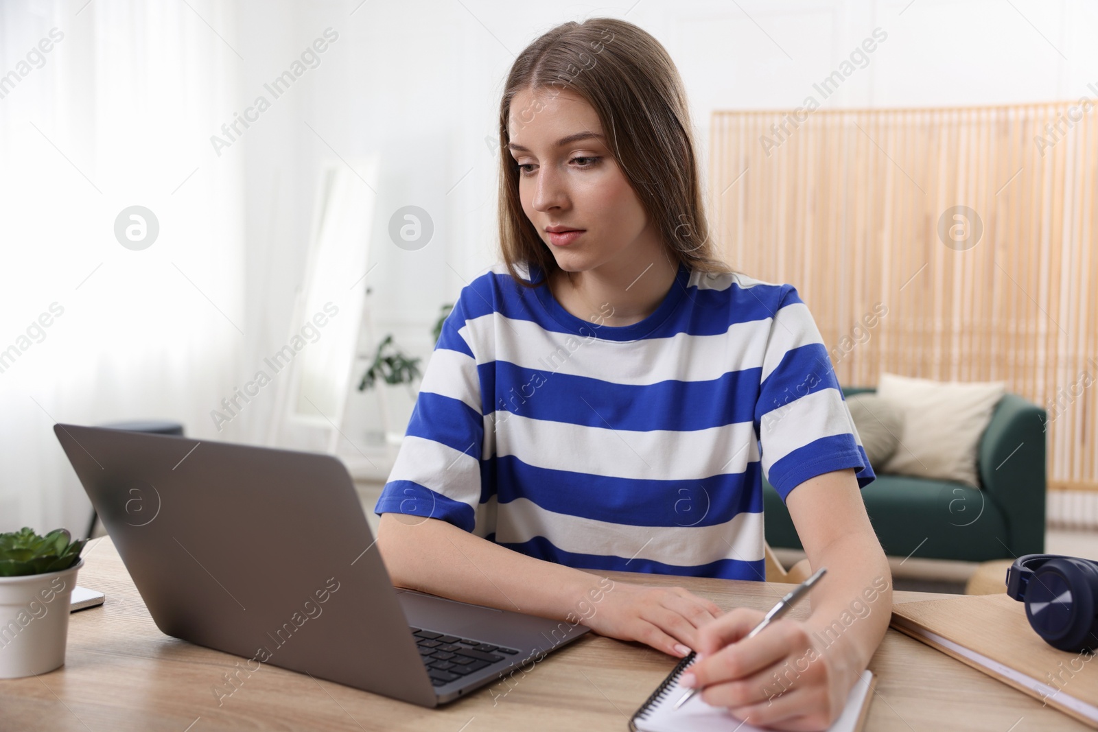 Teenage girl doing homework with laptop at wooden desk indoors Photo of Teenage girl doing homework with laptop at wooden desk indoors