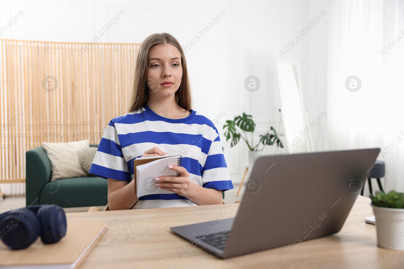 Photo of Teenage girl doing homework with laptop at wooden desk indoors