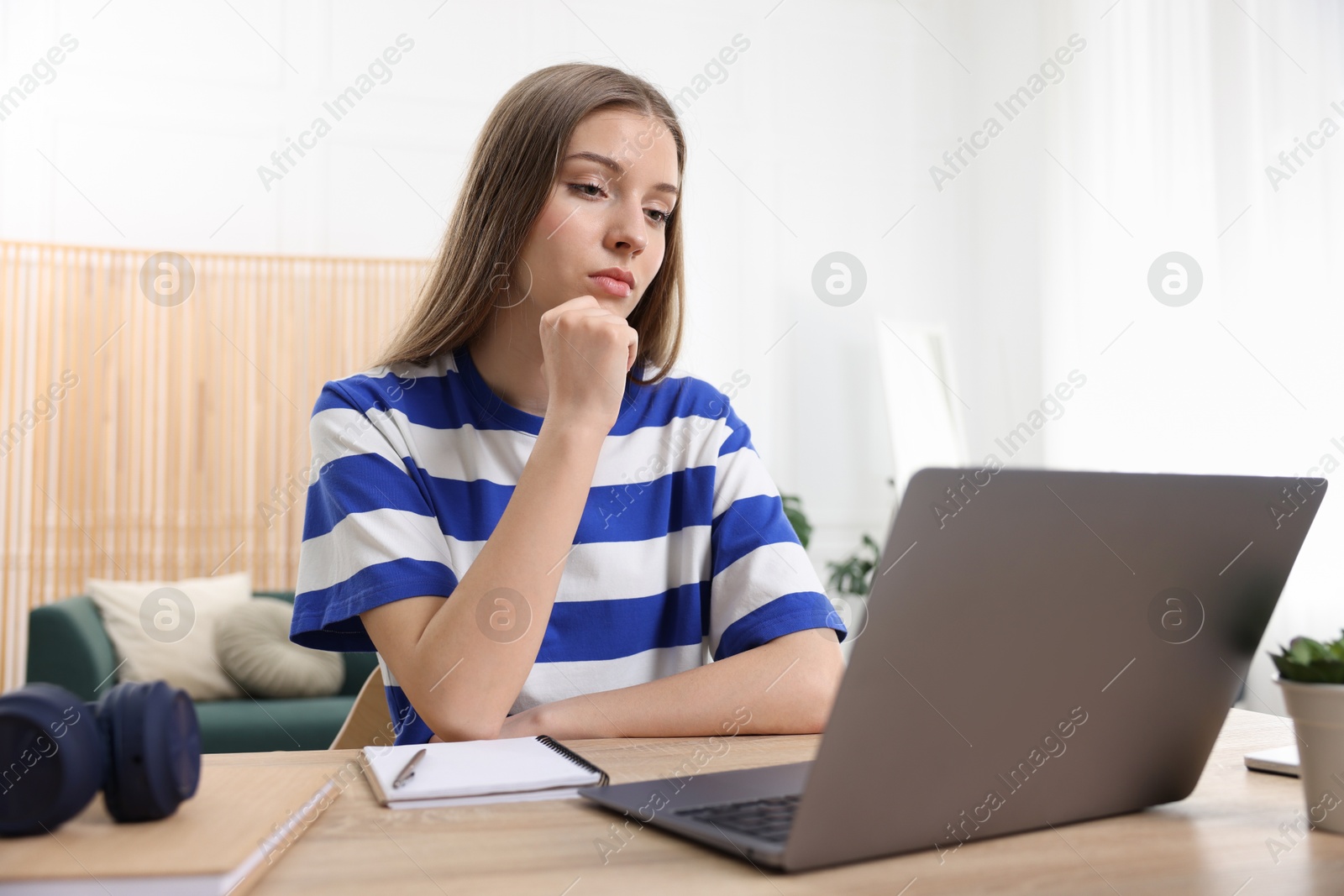 Teenage girl doing homework with laptop at wooden desk indoors Photo of Teenage girl doing homework with laptop at wooden desk indoors