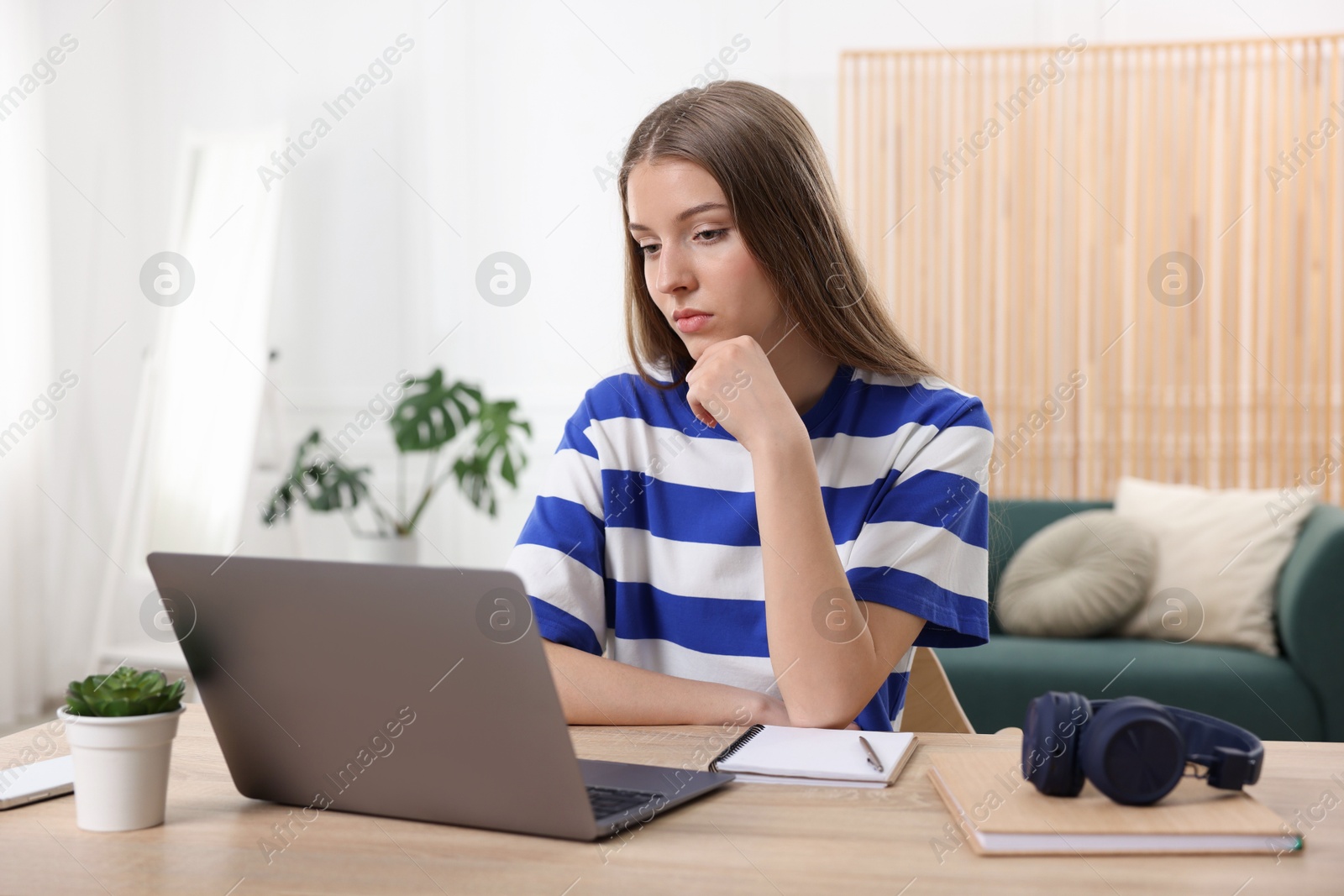 Teenage girl doing homework with laptop at wooden desk indoors Photo of Teenage girl doing homework with laptop at wooden desk indoors