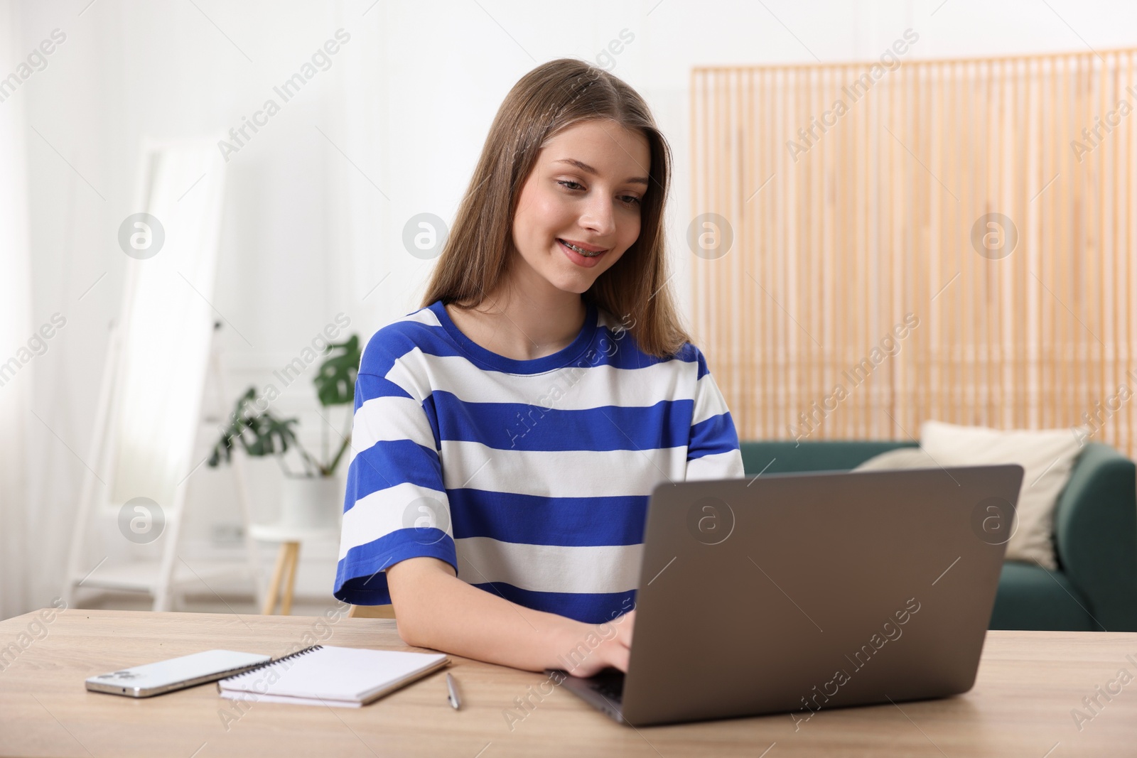 Teenage girl doing homework with laptop at wooden desk indoors Photo of Teenage girl doing homework with laptop at wooden desk indoors