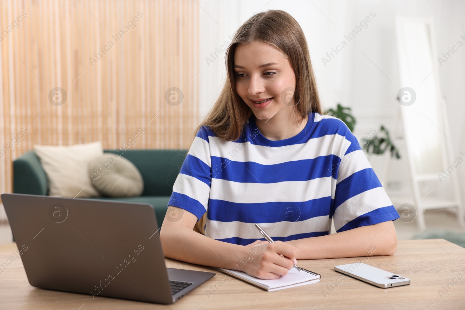 Teenage girl doing homework with laptop at wooden desk indoors Photo of Teenage girl doing homework with laptop at wooden desk indoors