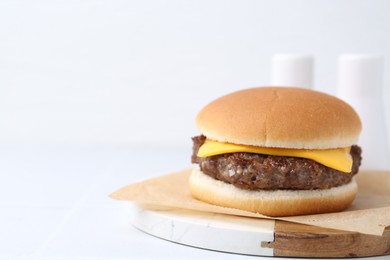 Photo of Tasty cheeseburger on white table, closeup. Space for text