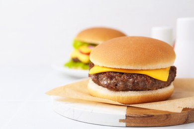Photo of Tasty cheeseburger on white table, closeup. Space for text