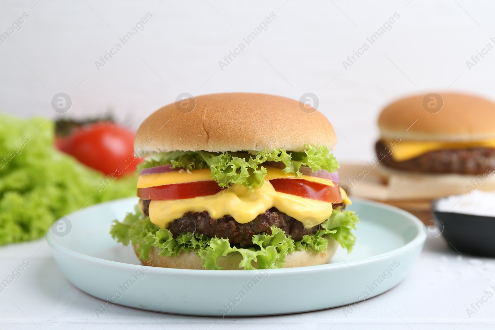Tasty cheeseburger with lettuce and tomatoes on white table, closeup Photo of Tasty cheeseburger with lettuce and tomatoes on white table, closeup