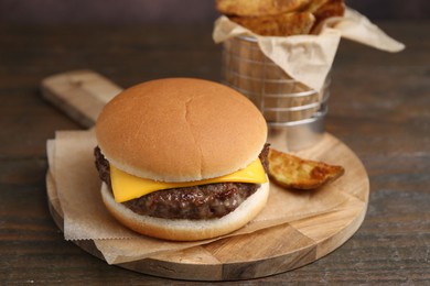 Photo of Tasty cheeseburger with potato wedges on wooden table, closeup