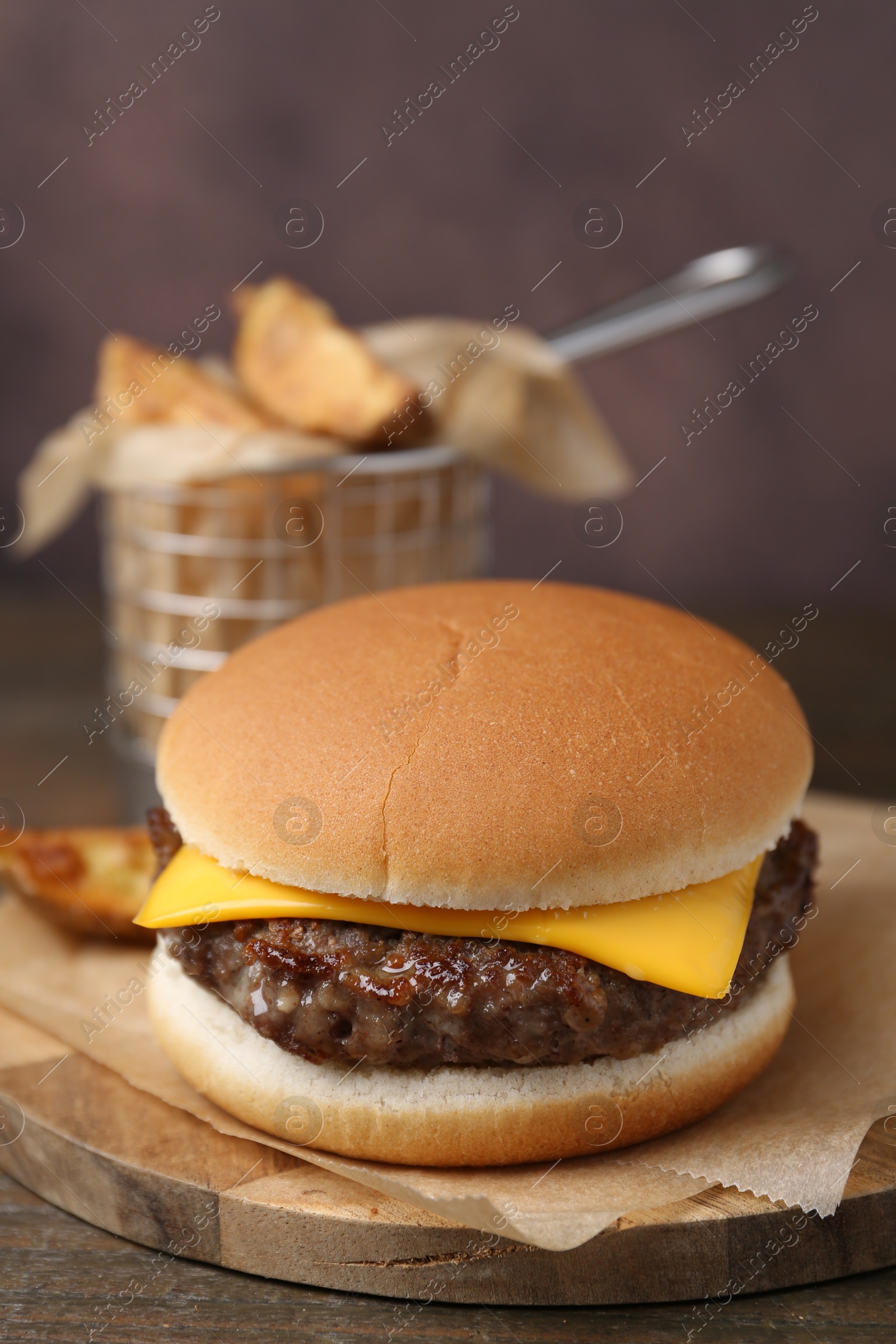 Tasty cheeseburger with potato wedges on wooden table, closeup Photo of Tasty cheeseburger with potato wedges on wooden table, closeup