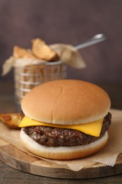 Photo of Tasty cheeseburger with potato wedges on wooden table, closeup