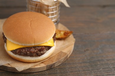 Photo of Tasty cheeseburger with potato wedges on wooden table, closeup. Space for text