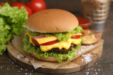 Photo of Tasty cheeseburger with potato wedges on wooden table, closeup