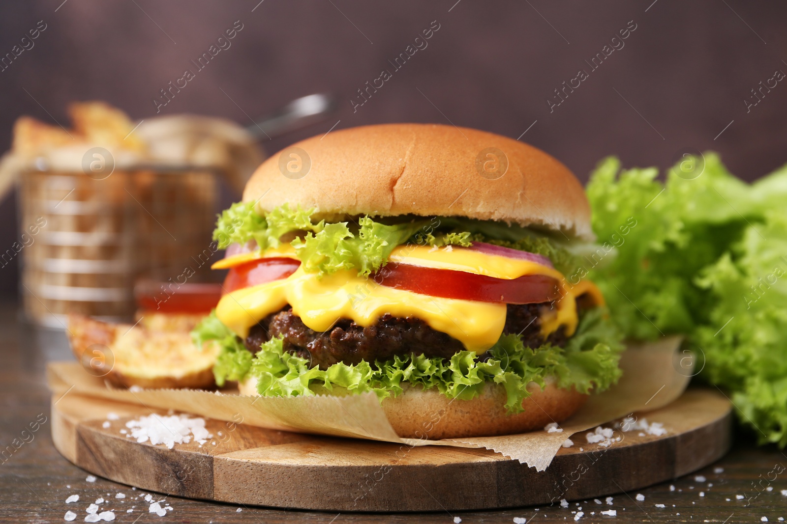 Tasty cheeseburger with potato wedges on wooden table, closeup Photo of Tasty cheeseburger with potato wedges on wooden table, closeup