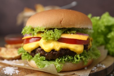 Photo of Tasty cheeseburger with lettuce and tomatoes on wooden table, closeup