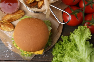 Photo of Tasty cheeseburger with potato wedges, ketchup and ingredients on wooden table, flat lay