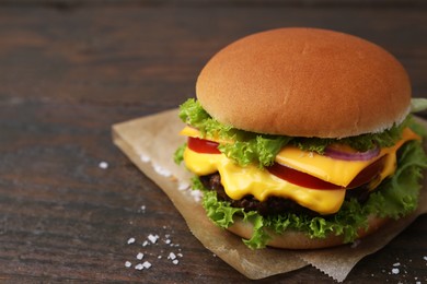 Photo of Tasty cheeseburger on wooden table, closeup. Space for text
