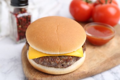 Photo of Tasty cheeseburger on white marble table, closeup