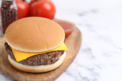 Photo of Tasty cheeseburger on white marble table, closeup. Space for text