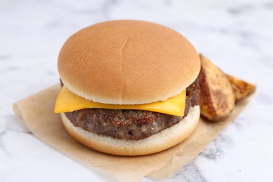 Photo of Tasty cheeseburger with potato wedges on white marble table, closeup