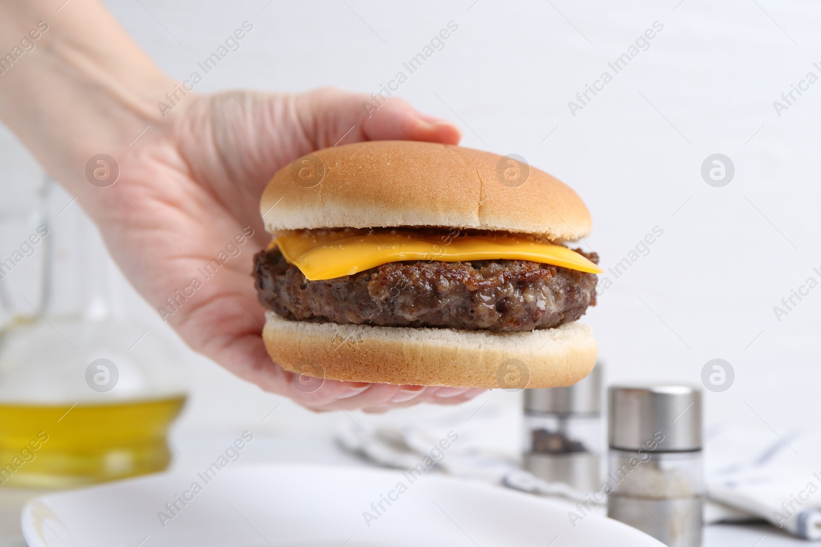 Woman holding tasty cheeseburger at white table, closeup Photo of Woman holding tasty cheeseburger at white table, closeup