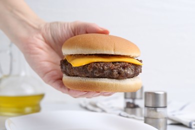 Photo of Woman holding tasty cheeseburger at white table, closeup