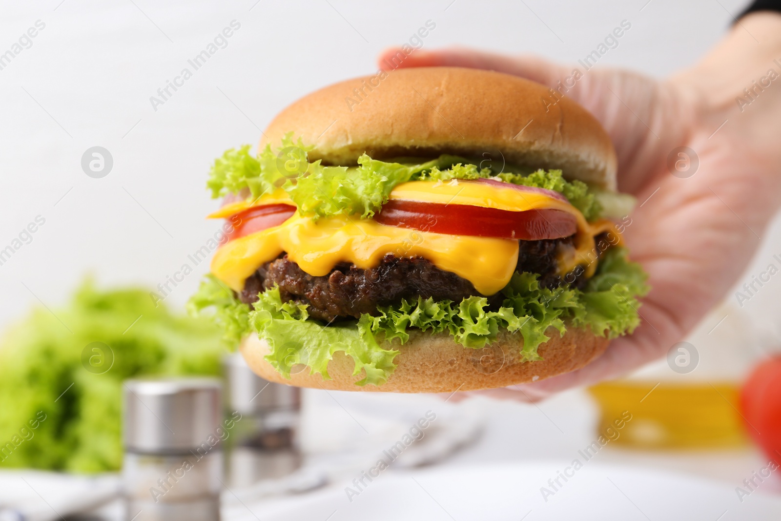 Woman holding tasty cheeseburger at white table, closeup Photo of Woman holding tasty cheeseburger at white table, closeup