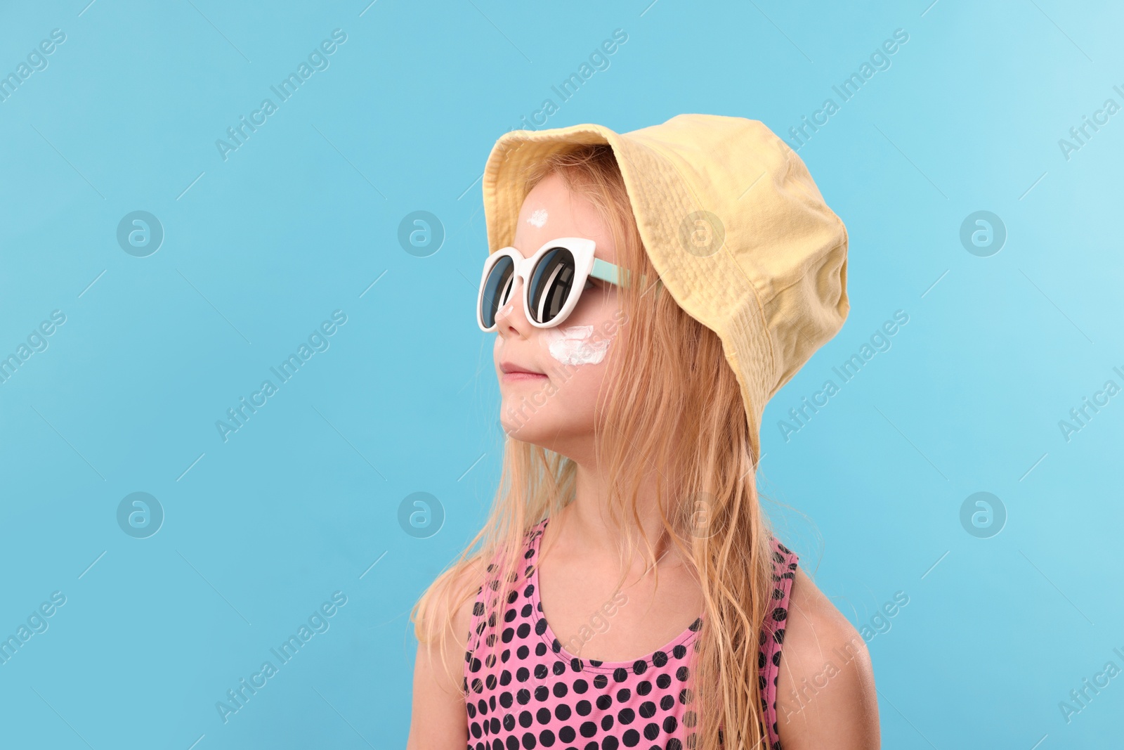 Cute little girl with sun protection cream on her face against light blue background. Space for text Photo of Cute little girl with sun protection cream on her face against light blue background. Space for text